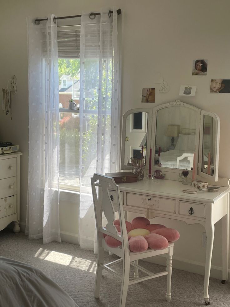 a bedroom with a desk, mirror and dresser in it's corner next to a window