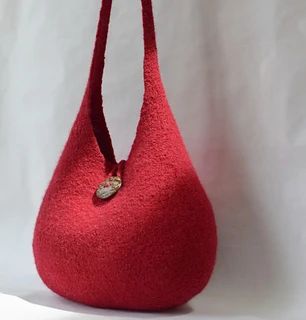 a red handbag with a gold button on the front and strap hanging from it