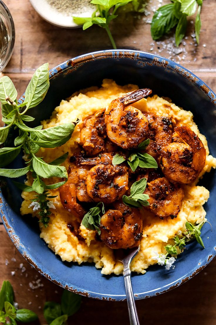 a blue bowl filled with shrimp and mashed potatoes on top of a wooden table