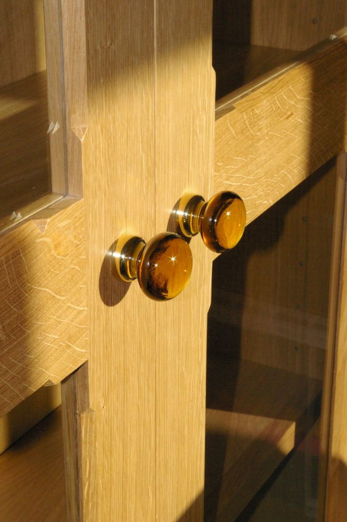 two glass knobs on a wooden cabinet door with sunlight coming through the window behind them