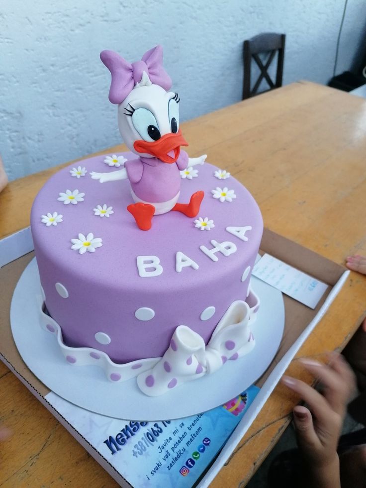 a purple cake with white polka dots and a pink donald duck figure on the top