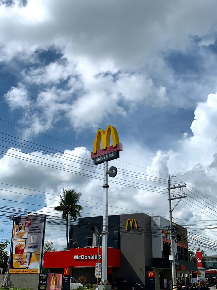 a mcdonald's restaurant on the corner of a street with palm trees and clouds in the background