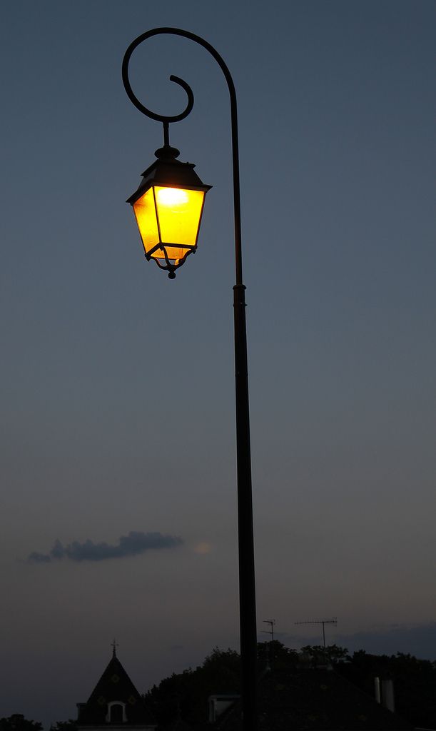 a lamp post with a building in the background at night time, lit by a street light