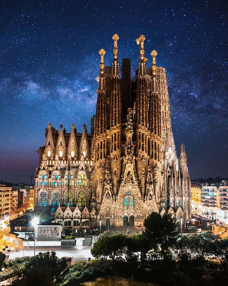 the cathedral is lit up at night with stars in the sky above it and buildings below