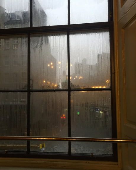 a window with rain falling down on the street and buildings in the backround