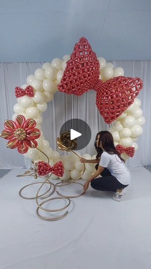 a woman kneeling down next to a giant balloon wreath with flowers and hearts on it