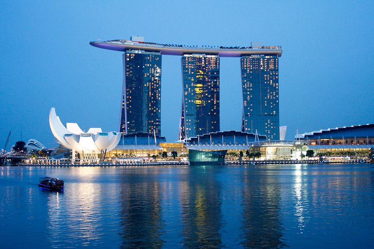 the city skyline is lit up at night with tall buildings in the foreground and boats on the water below