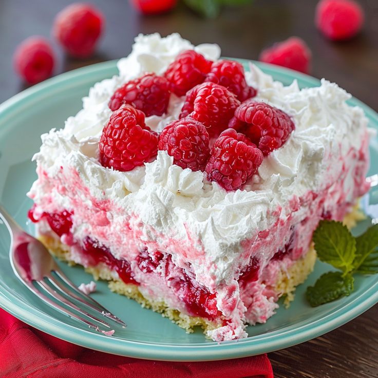 a piece of cake on a plate with raspberries and whipped cream frosting