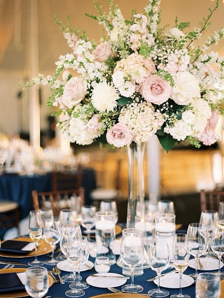 a tall vase filled with white and pink flowers on top of a blue table cloth