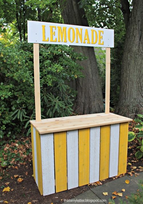 a lemonade stand with yellow and white stripes on the outside, in front of a tree