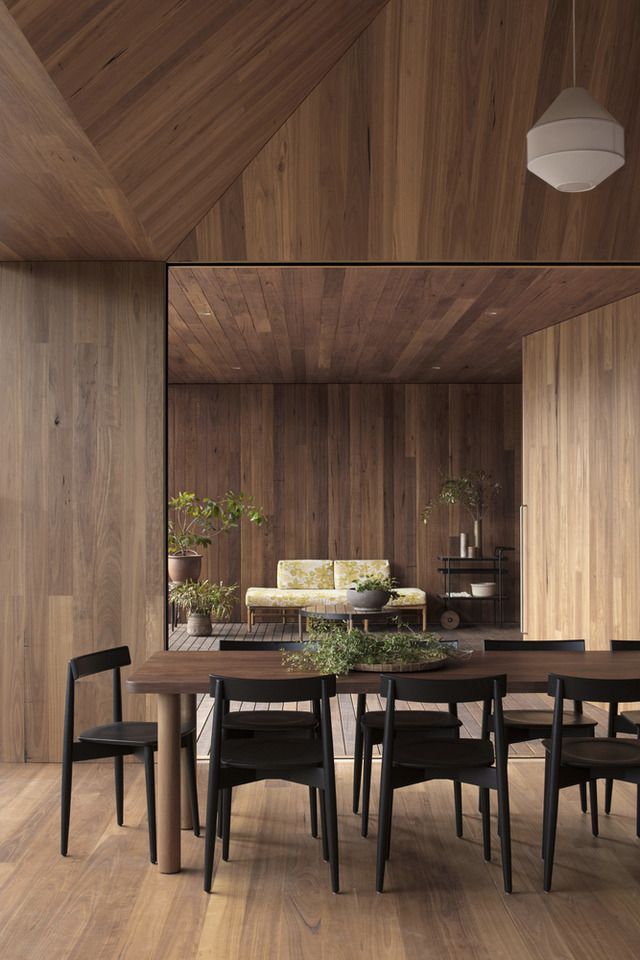 a wooden dining room table surrounded by black chairs and potted plants on top of it