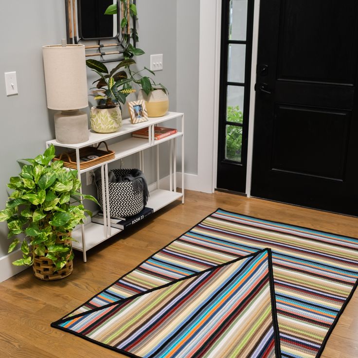 a living room with a rug, potted plant and black door in the background