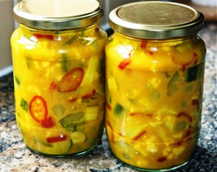 two jars filled with pickles sitting on top of a granite counter next to each other