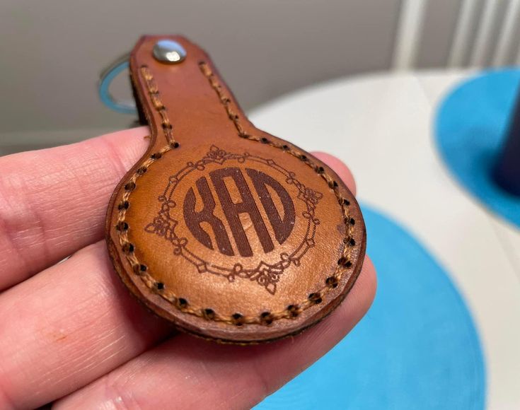 a hand holding a leather keychain with the initials on it