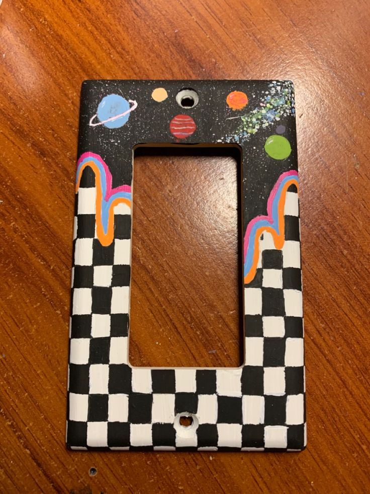 a black and white checkerboard light switch plate on a wooden table with an outer space theme painted on it