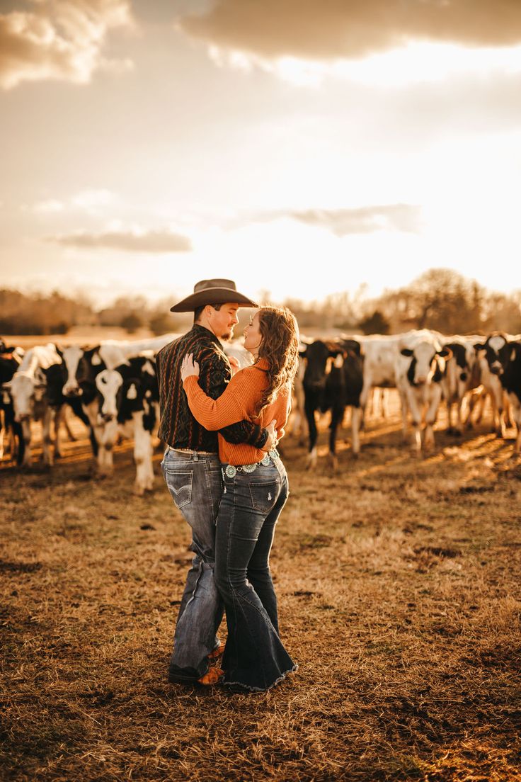 a man and woman are standing in front of cows on the field with their backs to each other