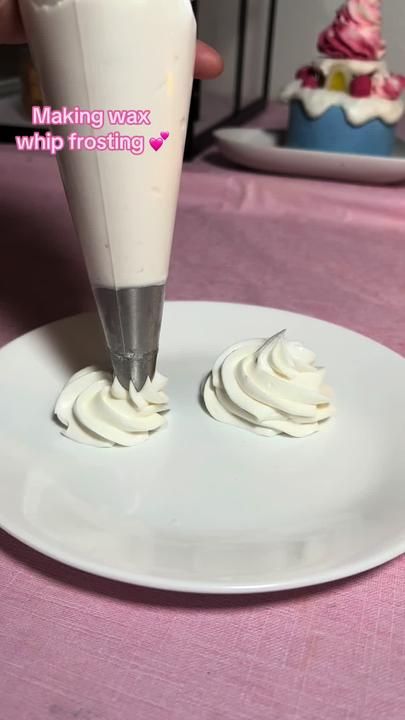 a person is making whipped cream on a white plate with pink table cloth and cupcakes in the background