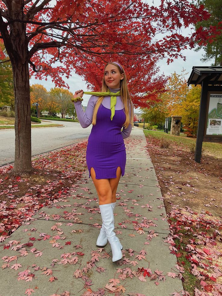 a woman in a purple dress and white boots is posing on the sidewalk with her back to the camera