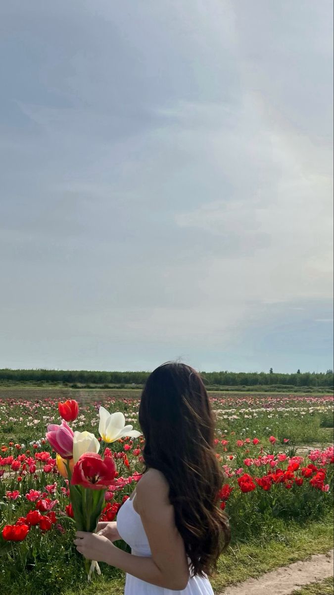 a woman in a white dress is walking through a field full of tulips