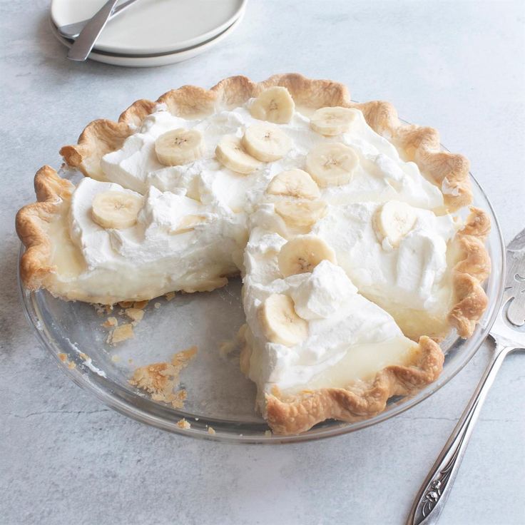 a banana cream pie sitting on top of a glass plate next to a knife and fork