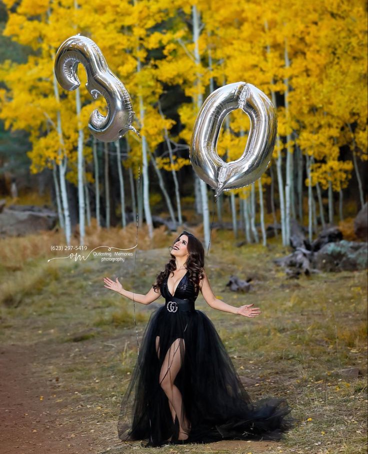 a woman in a black dress is holding two silver balloons