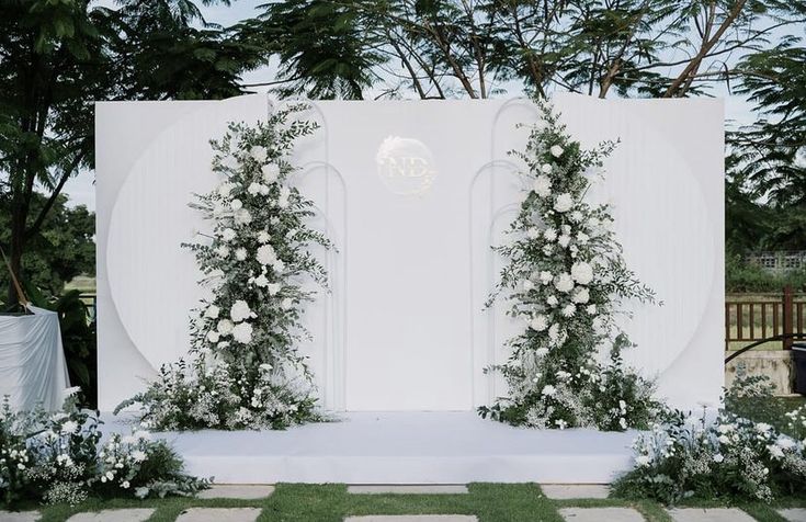 an outdoor ceremony setup with white flowers and greenery on the wall, surrounded by grass