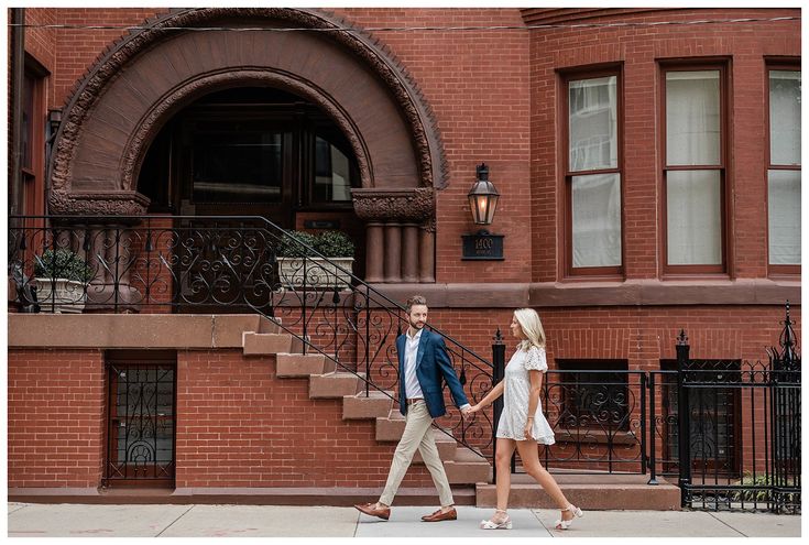 a man and woman walking down the sidewalk in front of a brick building holding hands