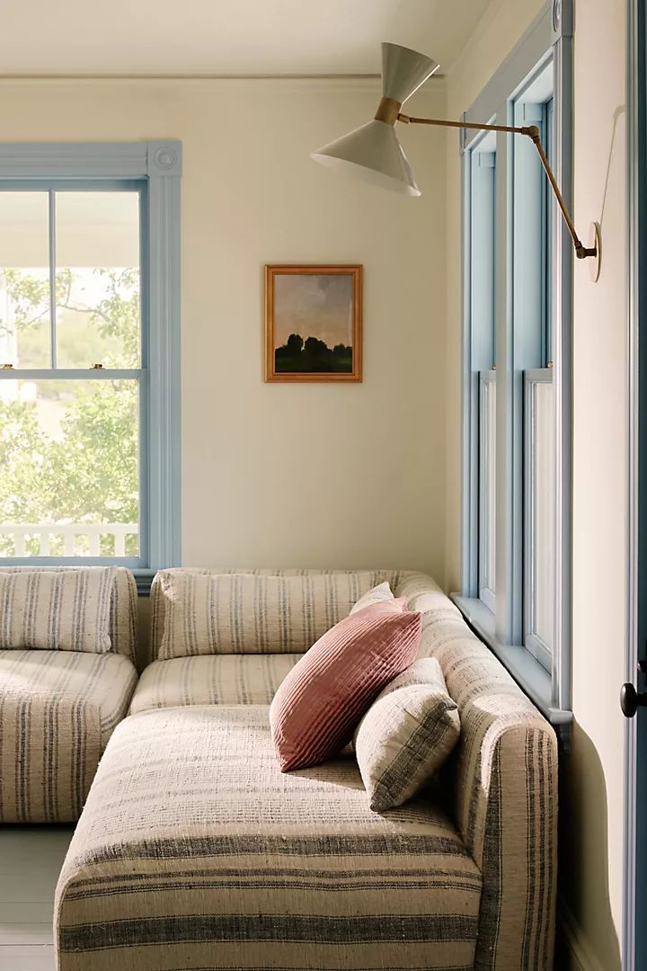 a couch sitting in front of a window next to a wall mounted light and a painting on the wall