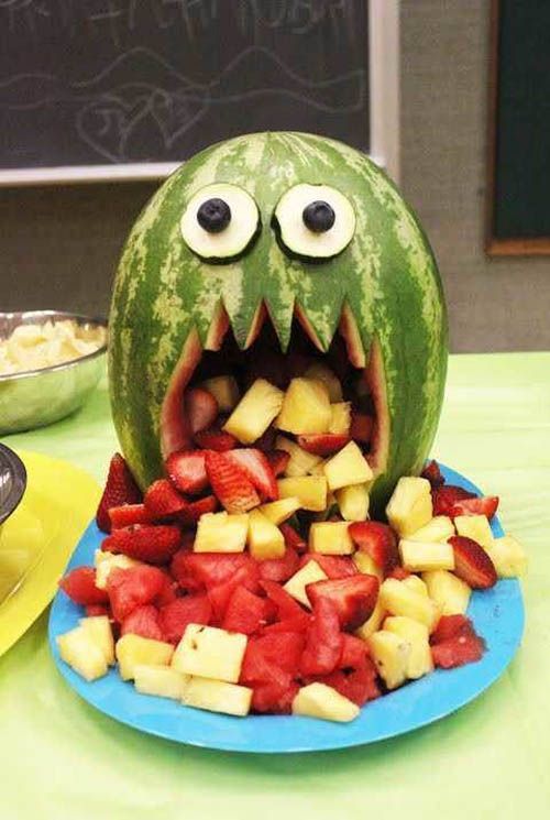 a watermelon shaped like a monster with its mouth open and fruit in the foreground