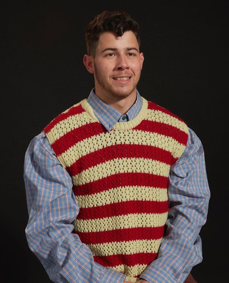 a man wearing a sweater and tie with his hands in his pockets, posing for the camera