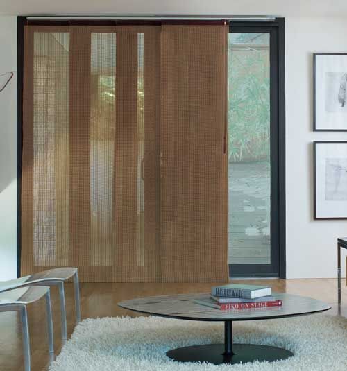 a living room with an area rug, table and sliding glass doors that have blinds on them