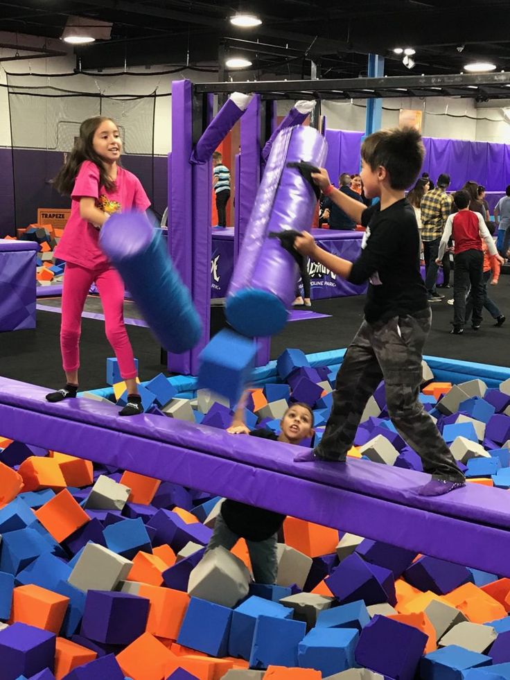 two children playing in an indoor play area with purple and orange blocks on the ground