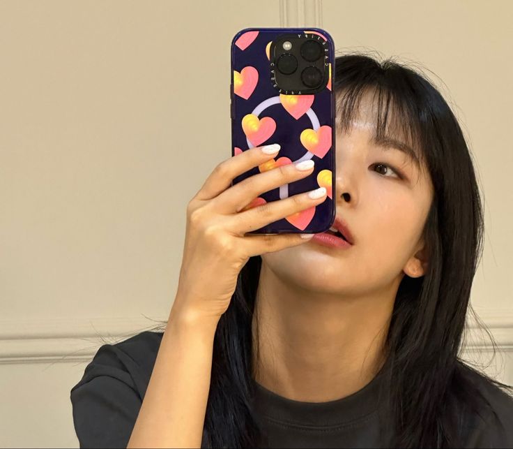 a woman taking a selfie with her cell phone in front of her face and wearing a black t - shirt