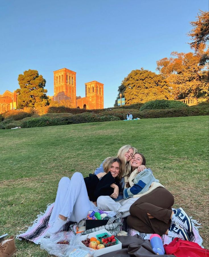 two women are sitting on a blanket in the grass with their arms around each other