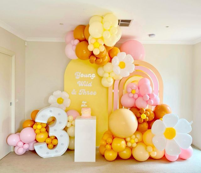 an arrangement of balloons, flowers and numbers are displayed in the corner of a room