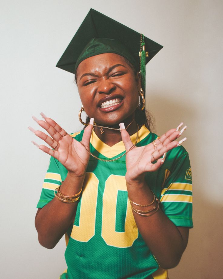 a woman wearing a green and yellow graduation cap making the vulcan sign with her hands