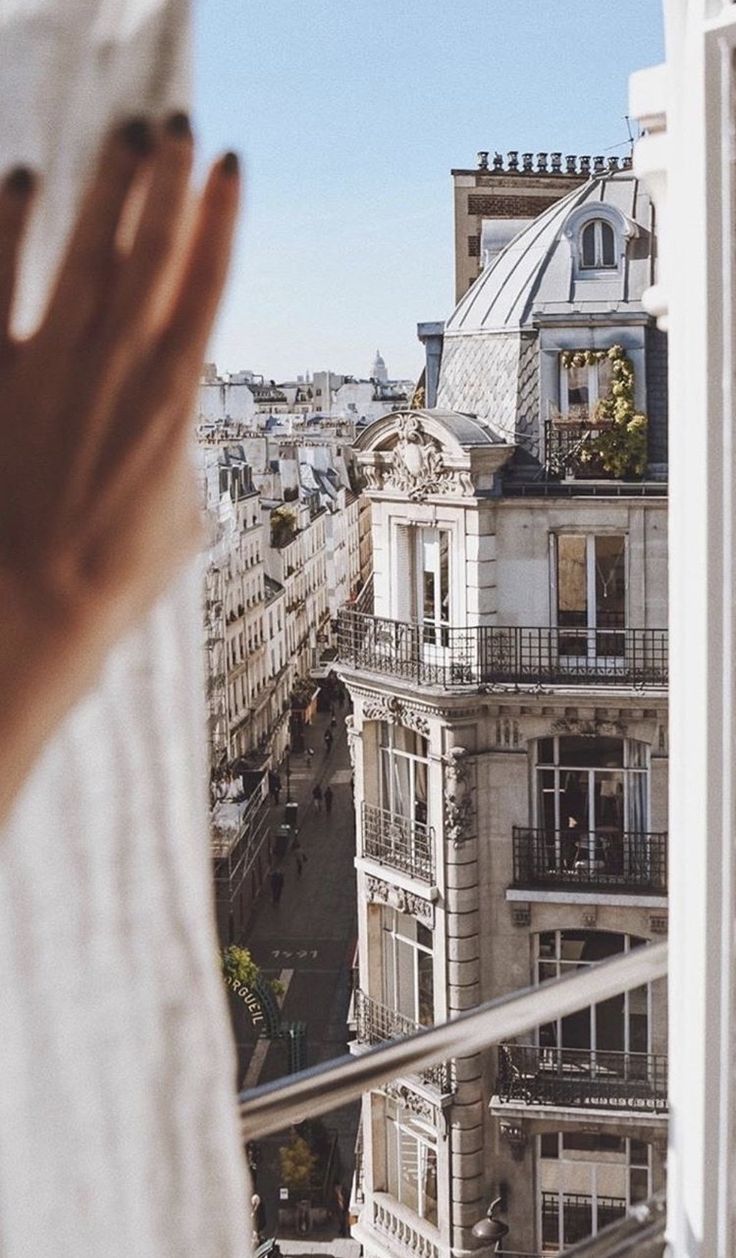 someone is looking out the window at some buildings and their hands are in front of them