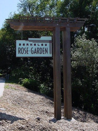 a sign for rose garden on the side of a road with trees in the background