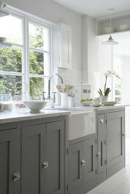 a kitchen filled with lots of white counter tops and gray cabinets next to a window