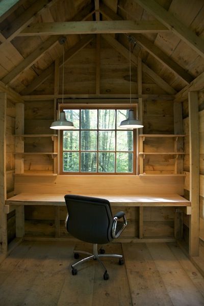 an empty desk in the corner of a room with wooden walls and ceiling beams, along with two hanging lights