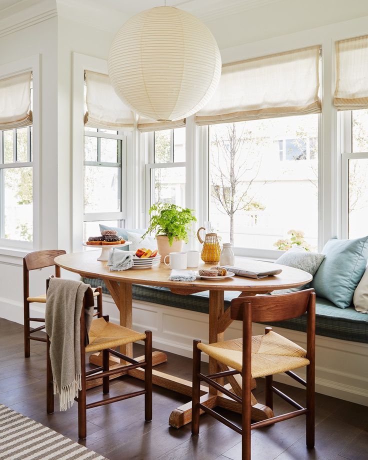 a dining room table with two chairs and a bench in front of the bay window