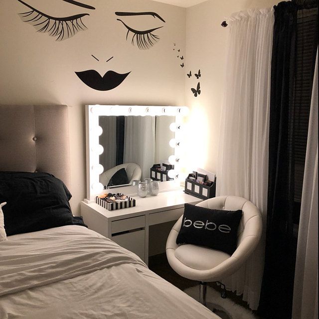 a bedroom decorated in black and white with eyelashes on the wall, makeup mirror, chair, and vanity