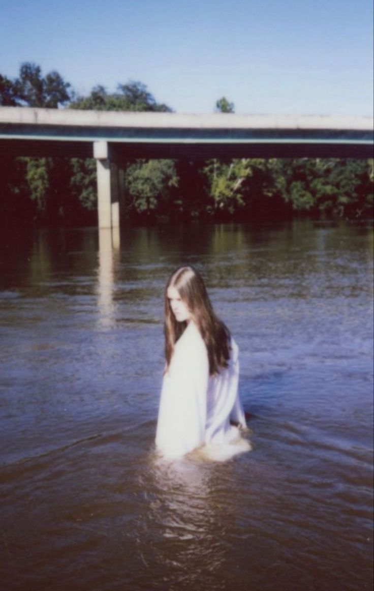 a woman standing in the water near a bridge