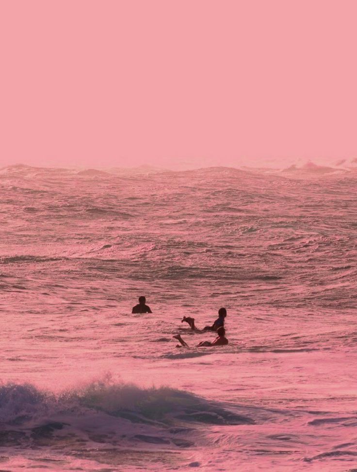 two people in the ocean on surfboards under a pink and purple sky at sunset