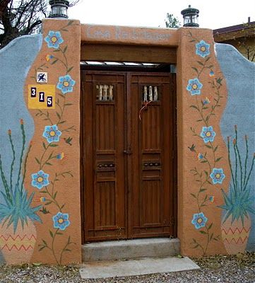 an adobe style building with flowers painted on the front and side walls, along with two wooden doors