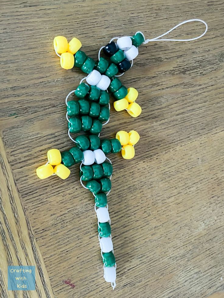 a green and yellow beaded cross sitting on top of a wooden table next to a string