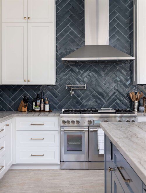 a kitchen with marble counter tops and white cabinets, stainless steel range hood over the stove