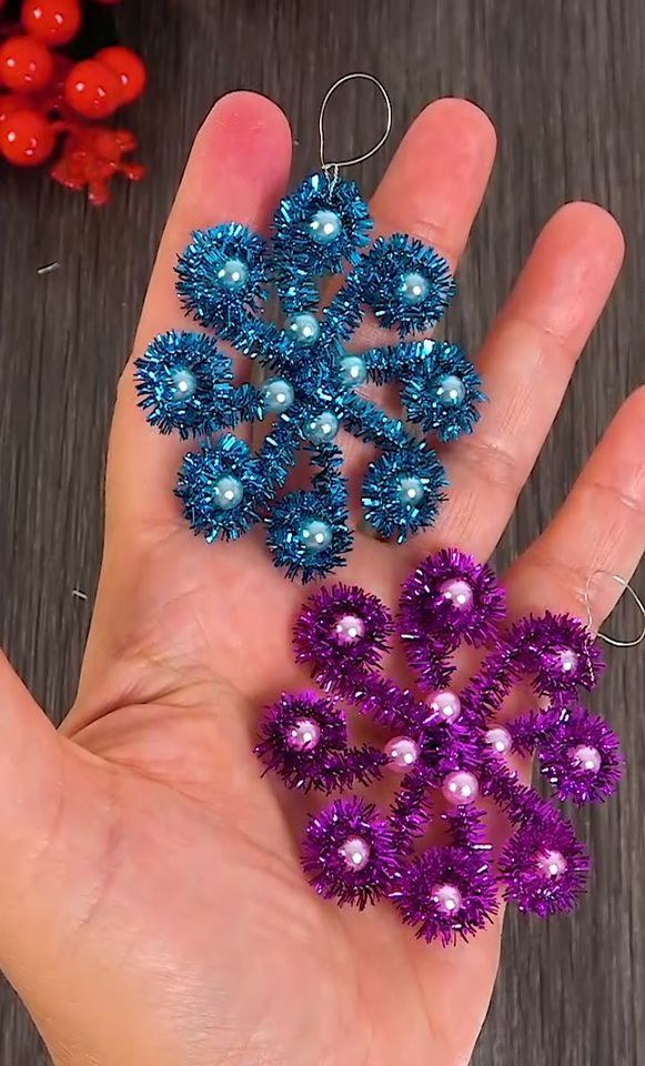 two handmade ornaments are being held by someone's hand on a table with other decorations in the background