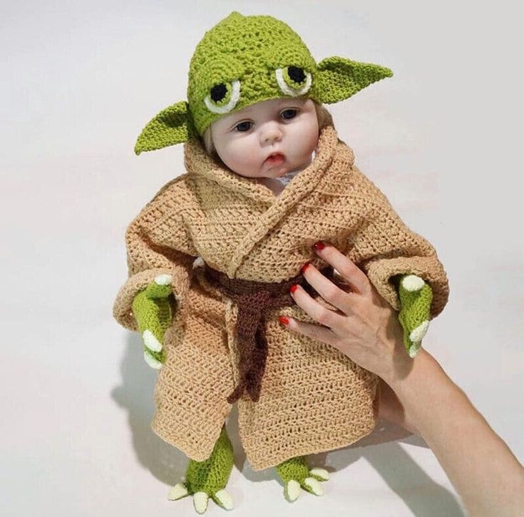 a baby in a knitted yoda outfit being held by someone's hand