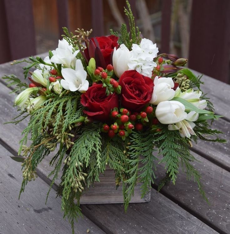 a bouquet of flowers sitting on top of a wooden table with greenery and berries